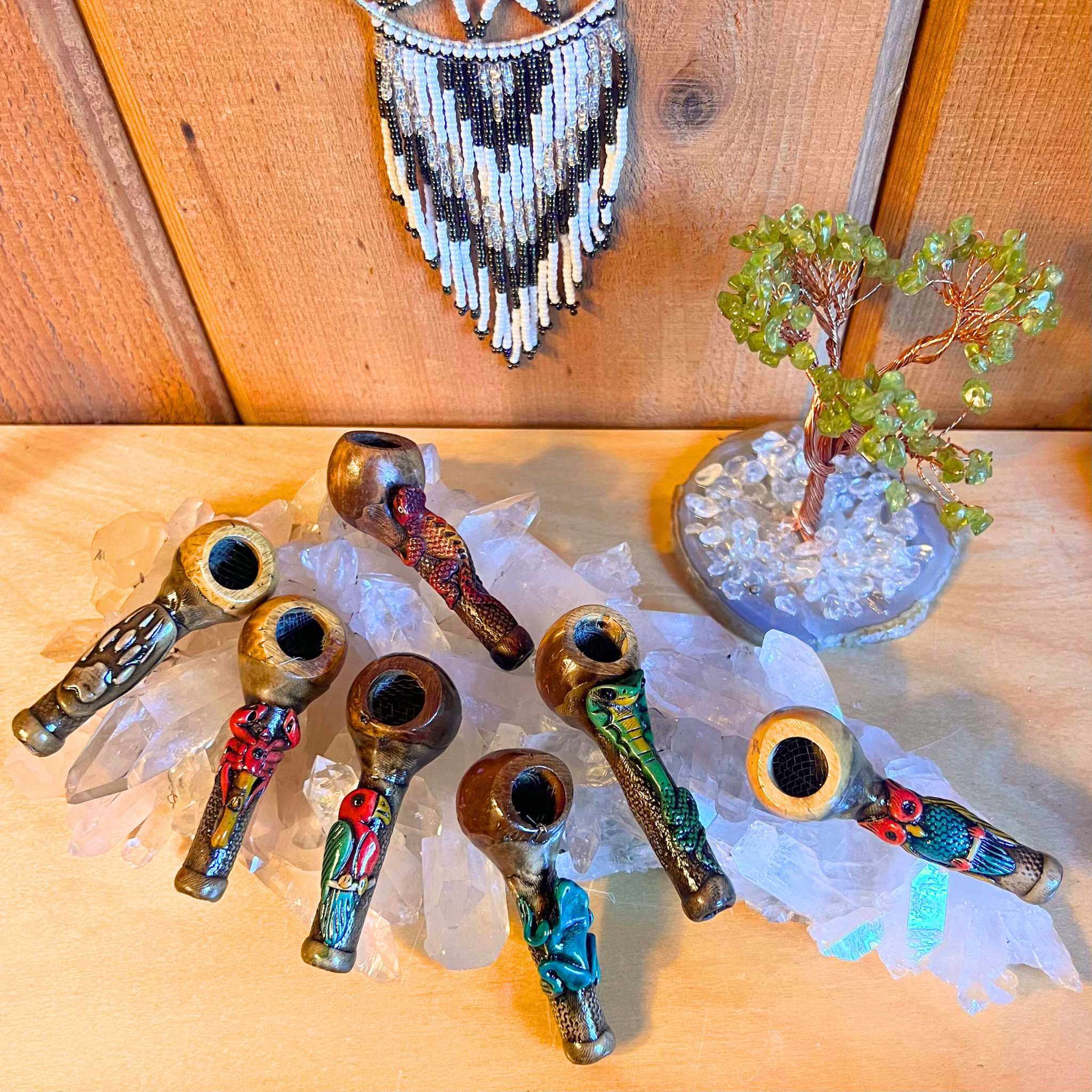 Handmade ceremonial pipes crafted from natural materials, each uniquely shaped and painted, arranged on crystals and wood.