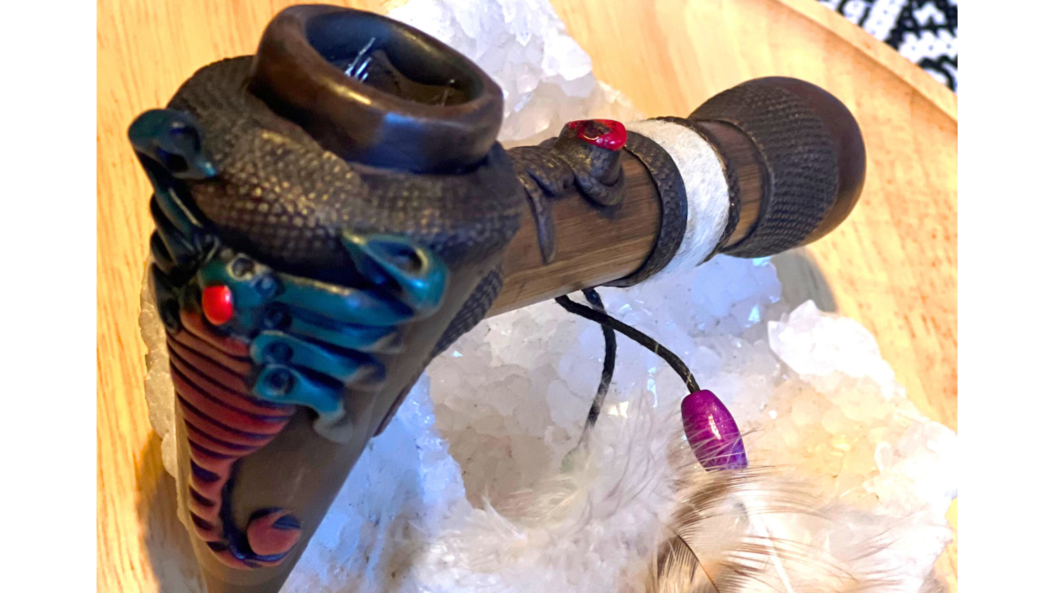 Black and colorful handmade ceremonial pipe with a feather attachments, placed on a white crystal 