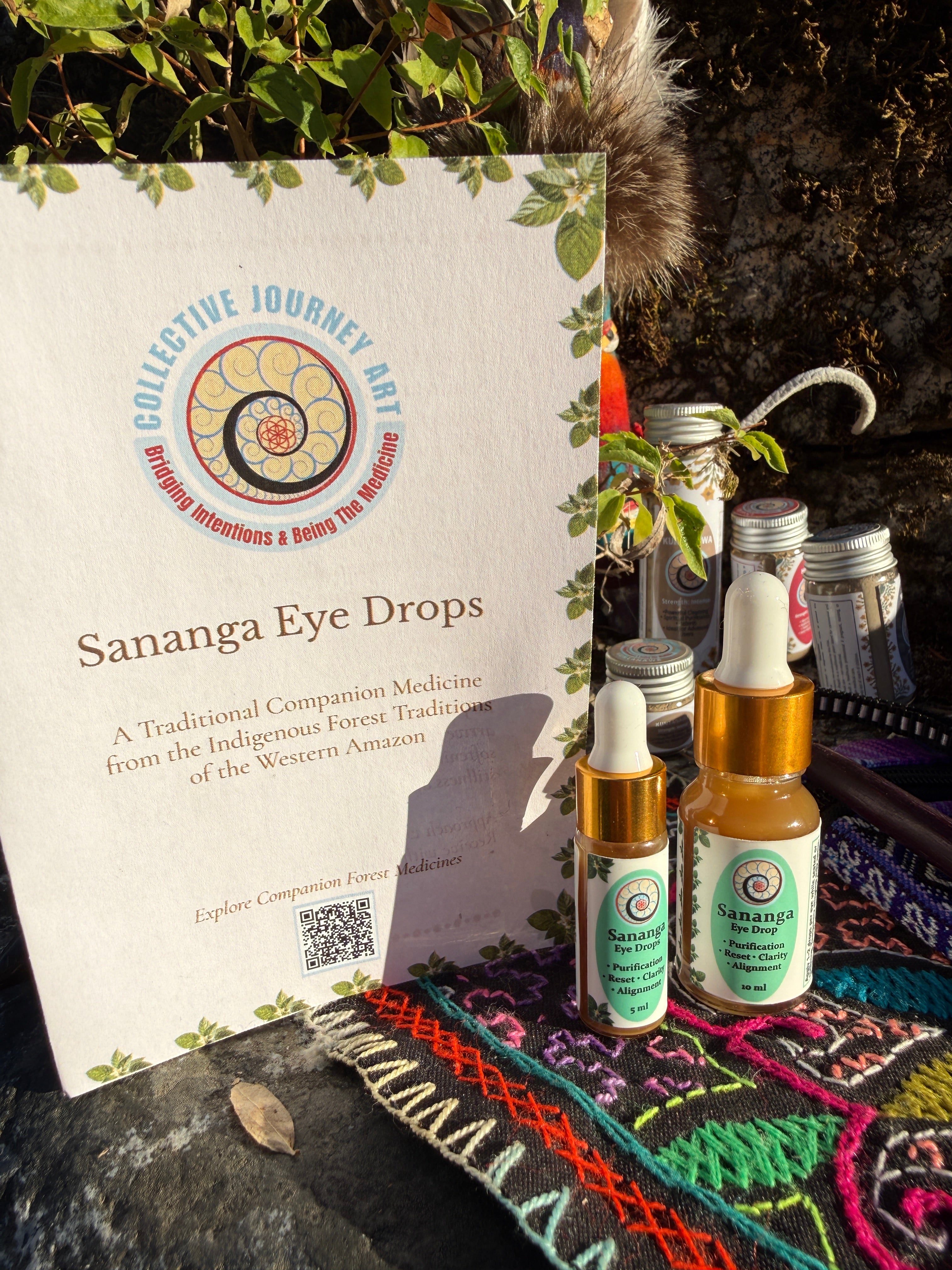 Collective Journey Art 5ml and 10ml Sananga Eye Drops bottles next to a traditional Western Amazon educational guide on a colorful, handwoven Shipibo textile.