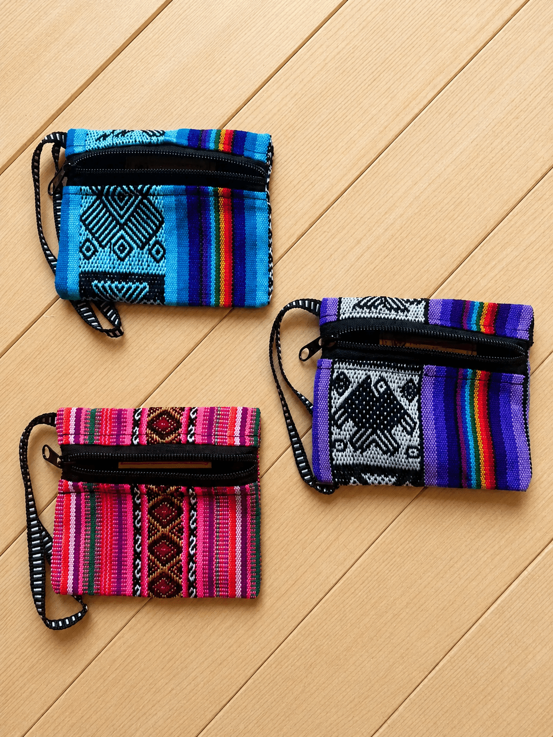 Three handcrafted mini zippered woven pouches by Collective Journey Art in blue, purple, and pink textile patterns, displayed on a natural wood surface.