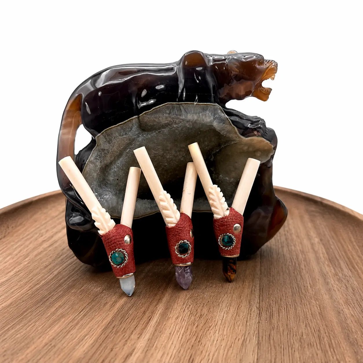 Handcrafted pelican bone crystal kuripe collection featuring moonstone, amethyst, tiger's eye, and chrysocolla gemstone variants displayed on a wooden tray with a carved stone bear sculpture.